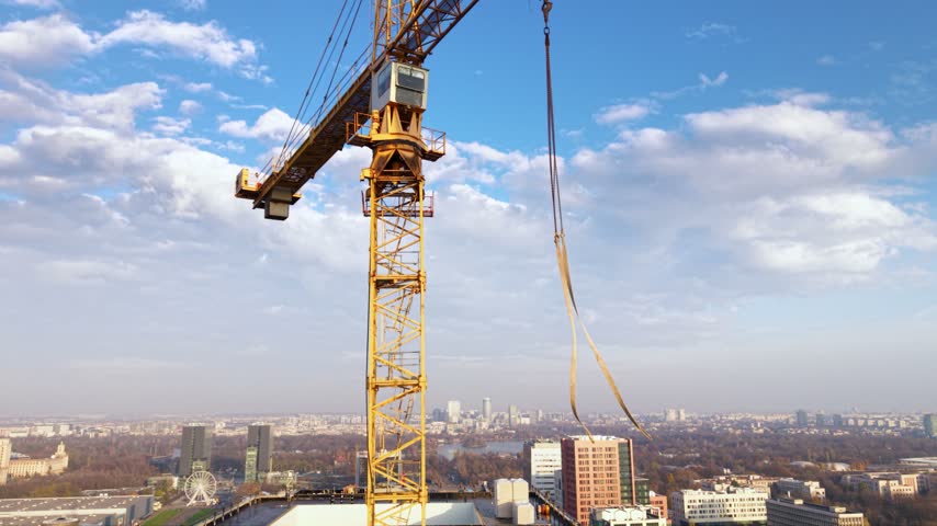 Aerial view of a large tower crane above a high-rise construction site in Bucharest, Romania, with modern office buildings, busy urban roads, residential districts and green parkland stretching across the city.