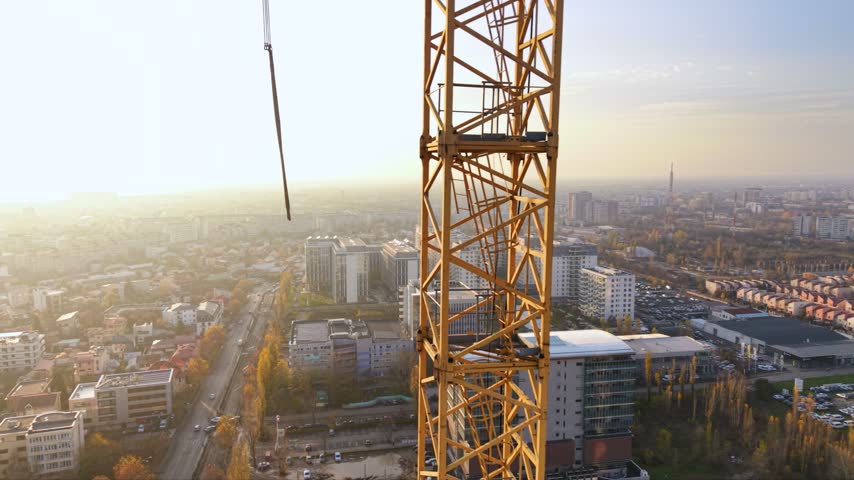 Aerial view of a large tower crane above a high-rise construction site in Bucharest, Romania, with modern office buildings, busy urban roads, residential districts and green parkland stretching across the city.