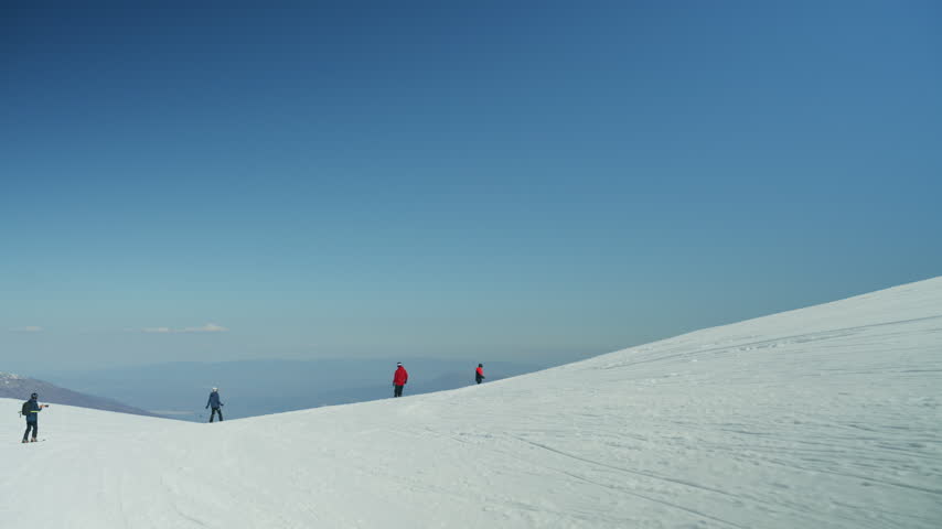 Three skiers are on a wide snowy mountain slope under a clear blue sky. The mountain landscape is bathed in bright sunlight, perfect for winter sports.