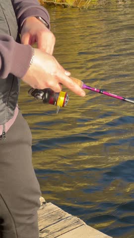 A person with light skin and short hair is fishing at a lake during autumn. The water reflects the colorful foliage around the shore.