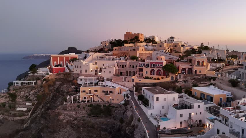 Golden hour light shines over the white traditional houses and cliffside buildings of Fira in the beautiful island of Santorini Greece