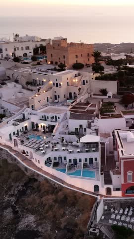 Golden sunlight shines over the white stone buildings and swimming pools of Fira in Santorini Greece during the peaceful twilight hours