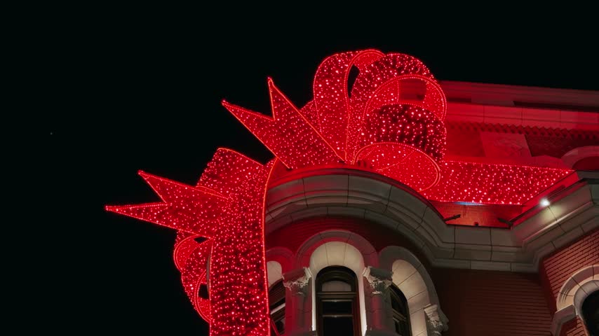 Vibrant red Christmas ribbon lights adorn a building in Thessaloniki, Greece, at night, showcasing authentic festive urban decorations during the holiday season.