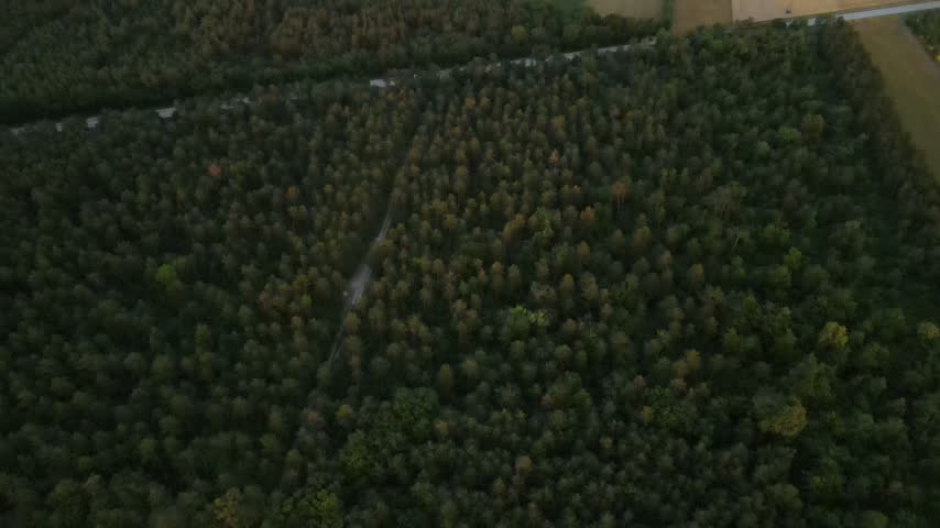Panoramic aerial view of agricultural fields, highway, and distant town at sunset.