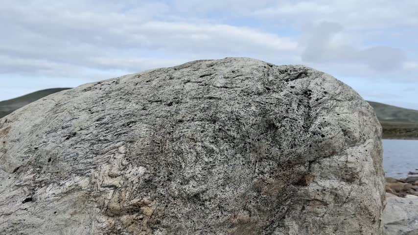 A large granite boulder in the foreground gives way to the calm surface of a mountain lake and the peaks of Dovrefjell.