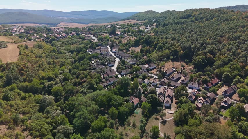Aerial view of the traditional village of Hollókő, Hungary, with clustered houses, winding roads, farmland and forested hills in the Cserhát Mountains.