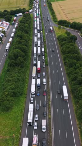 Aerial view of heavy traffic congestion on a dual carriageway with numerous trucks and cars lined up along the road surrounded by green fields and trees