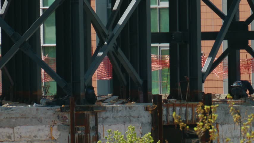Footage of professional welders working on structural steel beams at busy construction site with bright sparks flying.