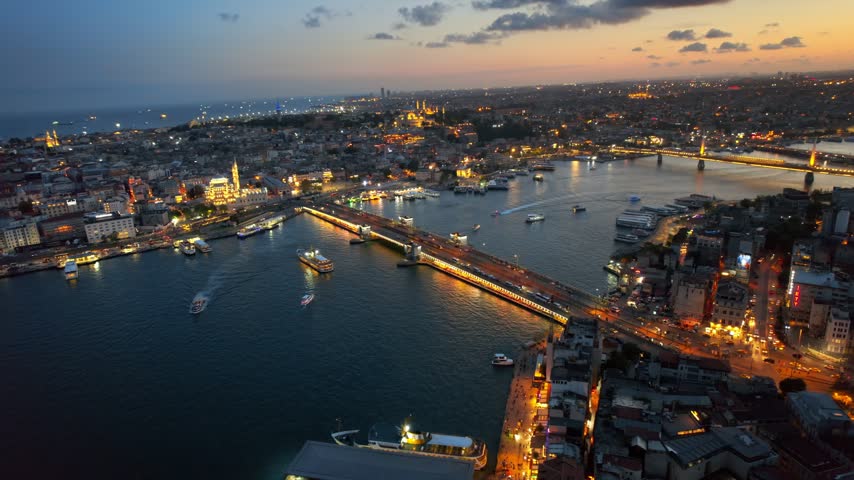 Panoramic view of illuminated Istanbul skyline featuring historic bridges, bustling maritime traffic, and sunset sky.