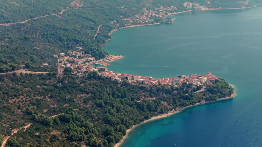 Drone shotcaptures Povlja’s red-roofed village nestled among lush hills, turquoise Adriatic waters, and rugged coastline.