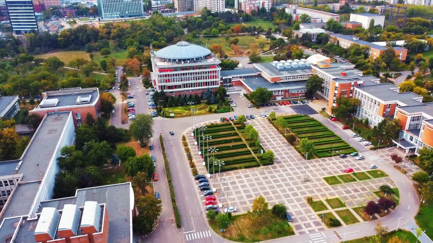 High angle aerial view of university campus buildings with garden landscape and parking lots in daylight, cinematic drone shot.
