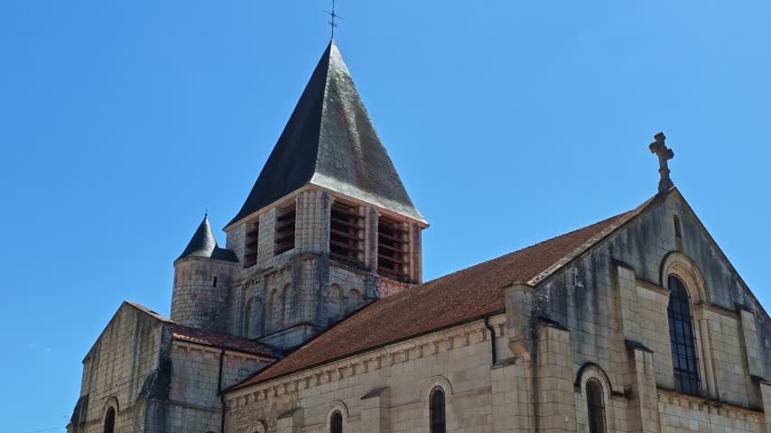 Notre Dame Church stands in Chauvigny, Vienne, Nouvelle-Aquitaine, France, showing Romanesque stonework, arched windows, sculpted portals and a prominent square bell tower, drone pan down.