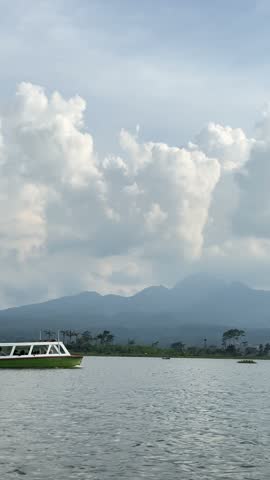 Scenic view of a boat on a serene lake with mountains and clouds in the background.