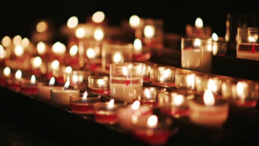 Candlelight glowing in dark cathedral setting. Rows of lit votive candles and tea lights flickering during ceremony.
