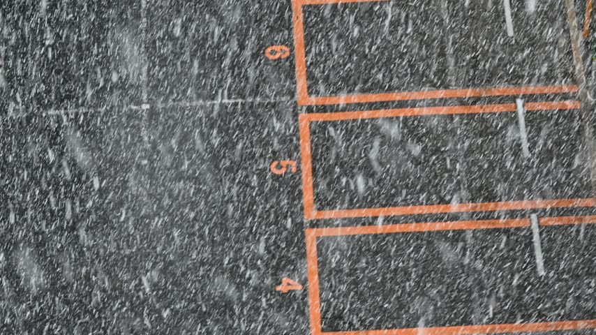 High angle aerial view of a snowy parking lot during a heavy blizzard with poor visibility.
