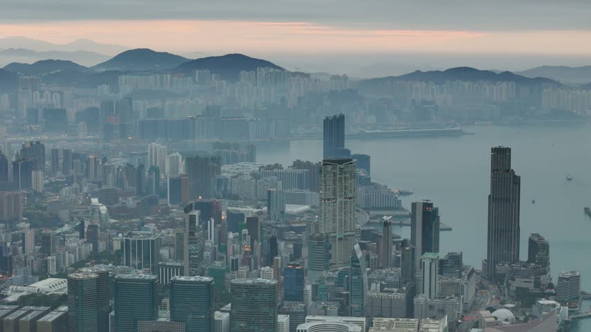Pastel morning cityscape: the camera glides above the skyscrapers as fog drifts over the far hills and the first pink light of day spreads along the Hong Kong horizon.