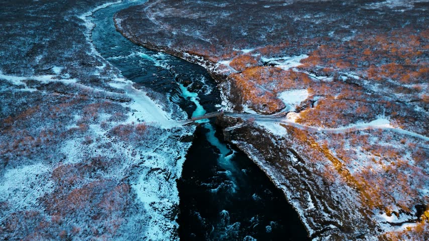 Aerial view of a river winding through snowy canyons and rugged Icelandic terrain