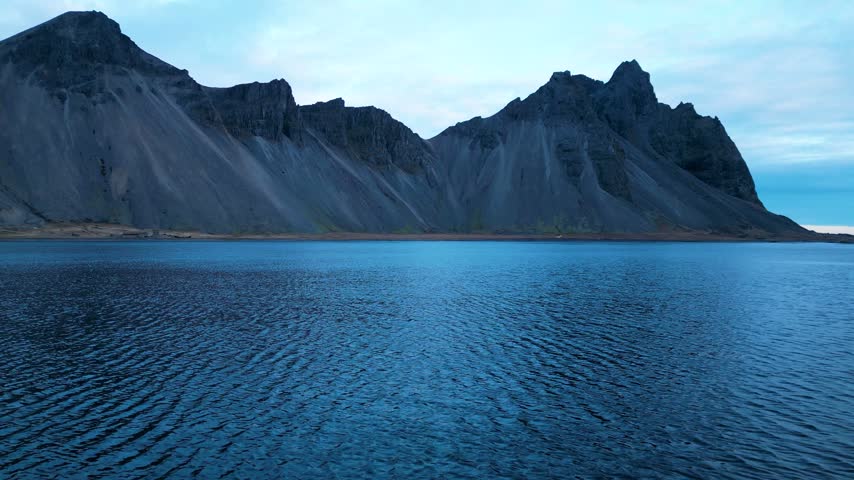 Wide view of rugged Icelandic mountains rising above calm blue coastal waters