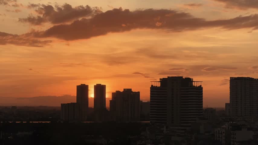 Golden sunset over modern city skyline with orange sky and silhouette buildings.