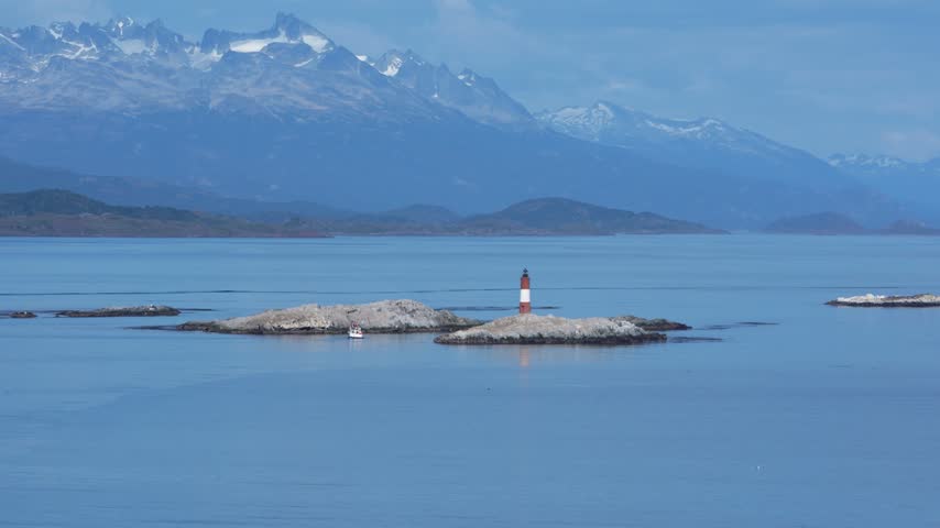Lighthouse on rocky island with snowy mountain backdrop
