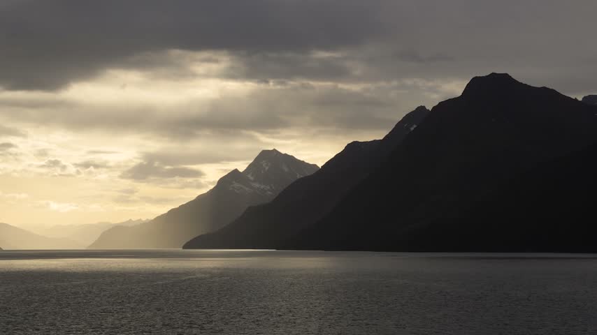 Serene mountain lake under cloudy sky with snow-capped peaks at dawn