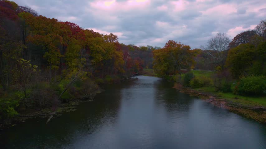 Low aerial drone view over calm lake water framed by colorful autumn trees at Mill Creek Park in Youngstown, Ohio.
