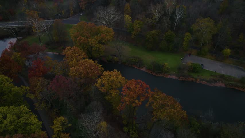 Drone view of Mill Creek Park in Youngstown, Ohio, featuring a calm river, winding roads, green lawns, and colorful autumn foliage.