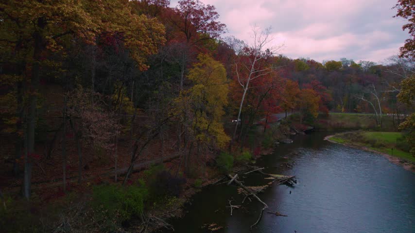 Stationary aerial view of a calm lake bordered by colorful autumn trees and wooded shoreline at Mill Creek Park in Youngstown, Ohio.