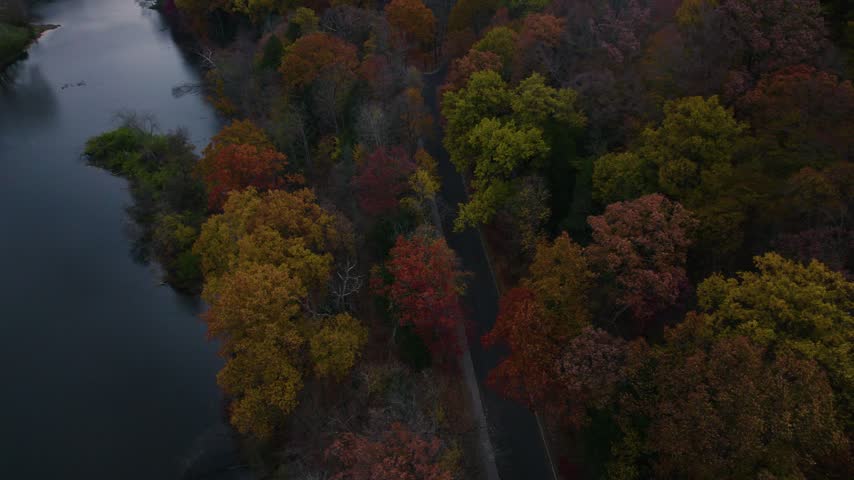 Drone view of a winding road through colorful autumn forest beside the water at Mill Creek Park in Youngstown, Ohio.