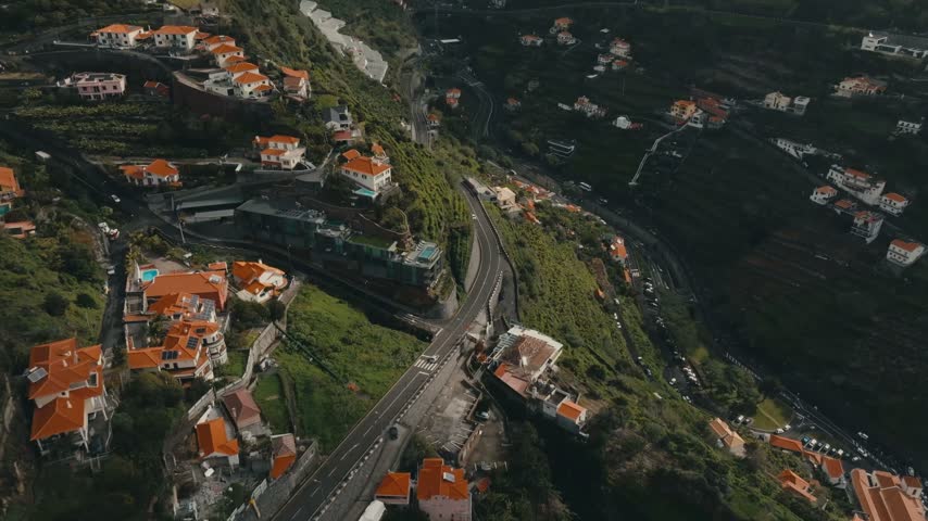 Mountain Landscape With Terraced Green Slopes, Winding Roads, And Houses With Terracotta Roofs In Madeira Island, Portugal. - aerial shot