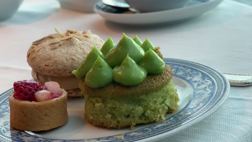 Assorted small cakes and pastries for tea, including a strawberry tart, green tea cake, and nut-topped macaron, arranged as delicate sweet treats for afternoon tea.