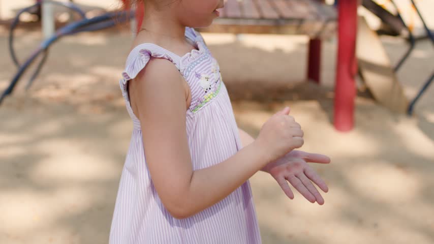 Two Asian girls play rock paper scissors outdoors at a sunny park playground.