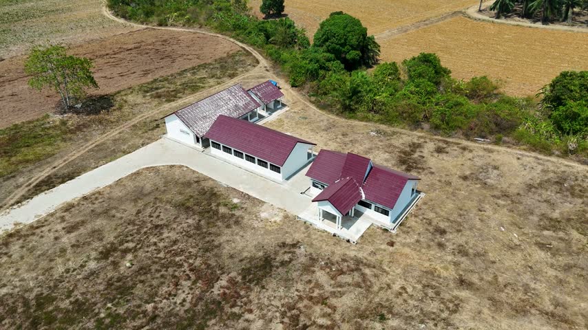 Aerial view of a rural Indonesian school with red roofs amid dry fields.