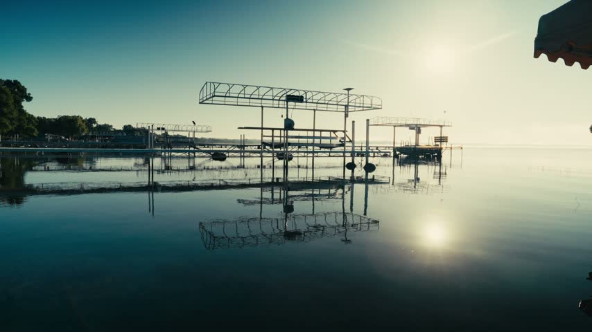 Wide angle shot of the morning sun over a calm lake with empty docks and boat lifts reflecting on the still water