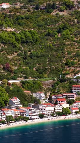 Croatia, aerial view of coastal village with red rooftops, green hills, and beach along the blue sea