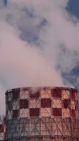 Massive cooling chimney discharges white water vapor into clear atmosphere. Power station maintains utility production as visible steam clouds billow steadily above patterned industrial stack.
