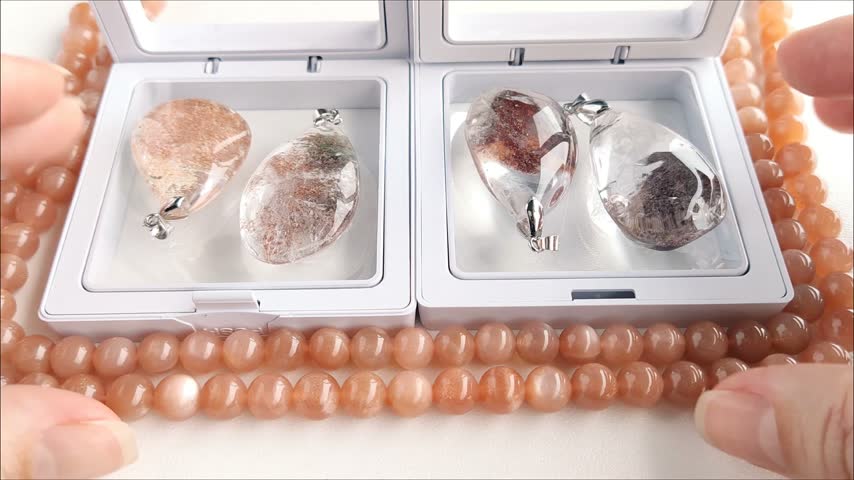 Detailed analytical examination of a transparent teardrop quartz pendant featuring distinct dark mineral inclusions, held against a backdrop of natural sunstone beads.