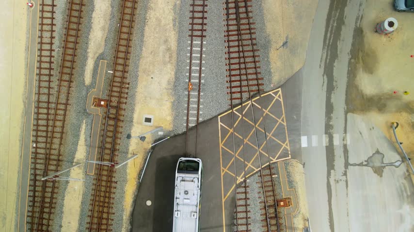 Top down view of parallel railway tracks beside a maintenance crew and parked vehicles at a train depot