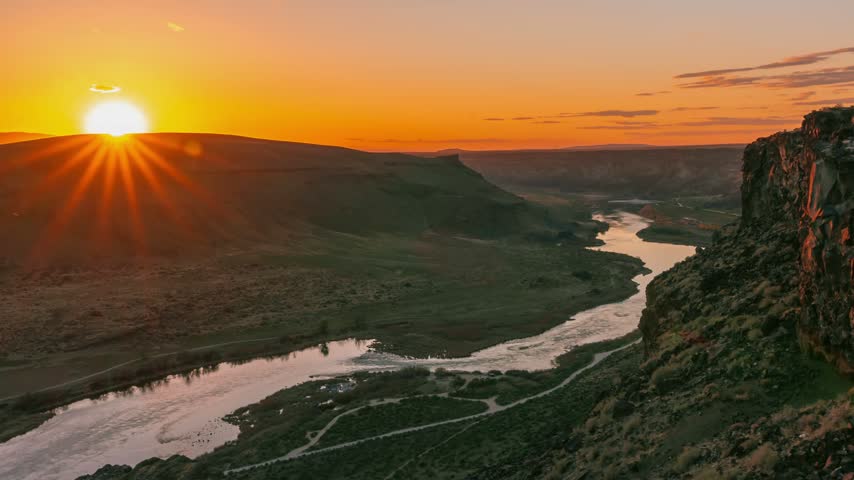 Idaho river winds through a deep rocky canyon during a vibrant sunset timelapse capturing the fading evening light over wild rural terrain