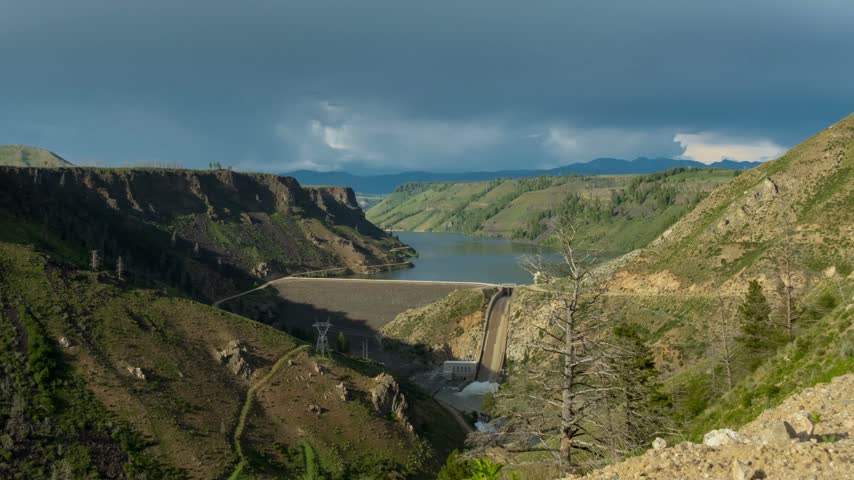 Reservoir dam nestled within a dramatic mountain canyon gorge during an overcast day capturing cascading water and wilderness landscape