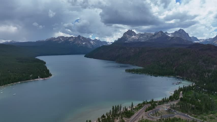 Stanley wilderness landscape viewed from above featuring a vast blue mountain lake surrounded by dense pine tree forests and dramatic rocky peaks under cloudy skies