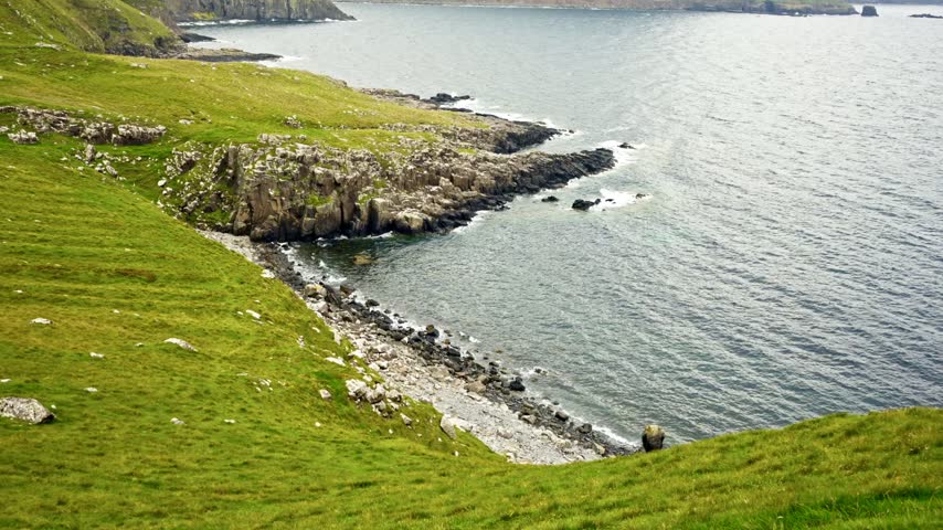 Lush green coastal cliffs overlook rugged rocky shorelines and calm blue gray waters along the scenic Isle of Skye in Scotland UK