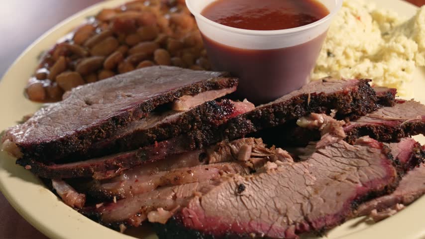 Mouthwatering close-up shot of lean, sliced brisket showcasing smoky bark and vibrant smoke ring, served with barbecue sauce, creamy potato salad, and beans on a rustic plate. Slider, 4K