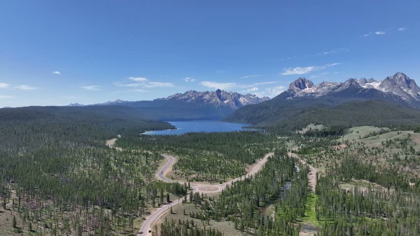 Stanley Idaho landscape showcases a winding forest road leading toward scenic alpine lakes and majestic Sawtooth peaks