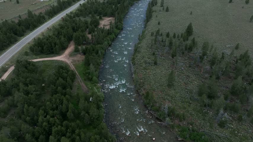 River flows through a lush forested valley alongside a highway in Stanley Idaho revealing mountain ranges in this scenic landscape