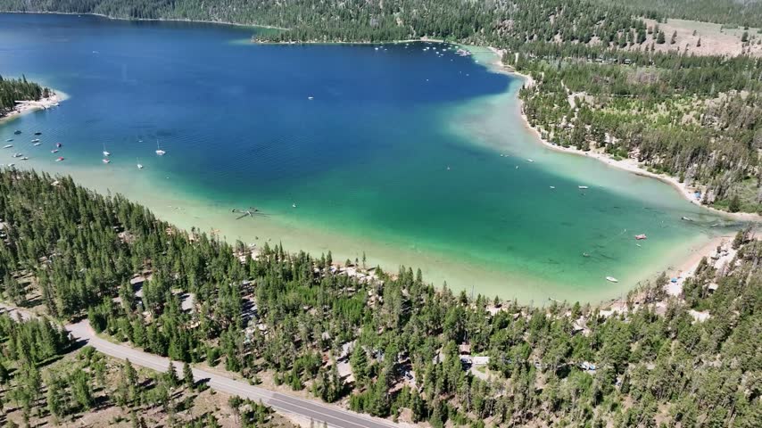 Stanley Idaho alpine lake features vibrant turquoise waters and green pine shores with dramatic mountain peaks under a sunny sky