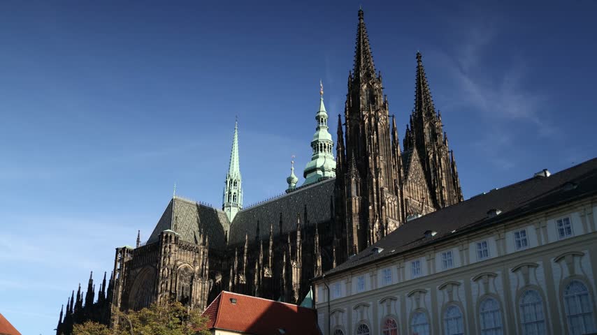 St Vitus Cathedral rises above Prague Castle with towering Gothic spires ornate stone details and historic palace buildings under a clear blue sky in the heart of the Czech capital