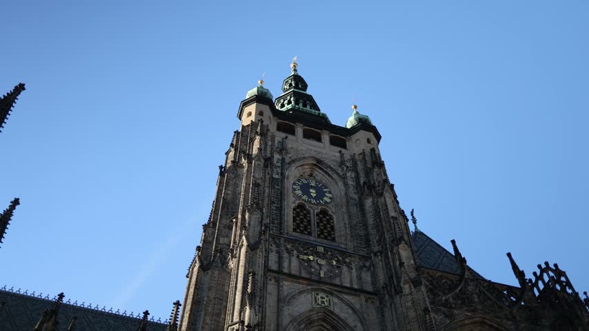 Prague Castle historic Gothic cathedral clock tower rises above ornate stone architecture with copper rooftops and medieval details against a clear blue sky in the Czech capital city