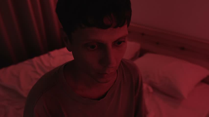 Anxious man experiencing a panic attack, breathing rapidly before holding his chest and slowing his breath to regain calm, showing anxiety and emotional distress in red low key lighting