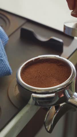 Barista tamping freshly ground coffee inside an espresso portafilter using a professional coffee tamper